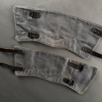 two pairs of gray cloth with black leather straps on a gray surface