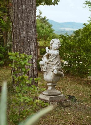 une statue représentant une femme assise sur un socle dans un jardin