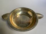 un plat ancien en argent posé sur une table blanche, muni d'une poignée en argent