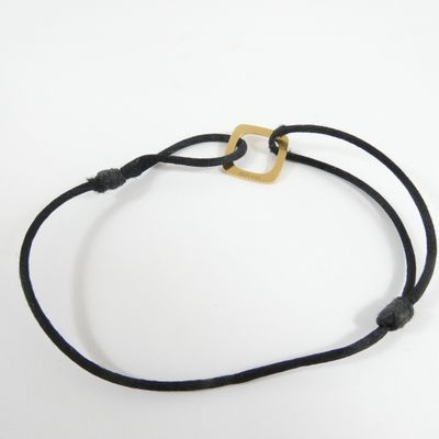 a close up of a black cord bracelet with a gold square on it