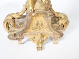 a gold clock on a stand on a white surface