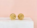 a pair of gold coin stud earrings sitting on top of a marble block