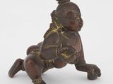 une petite figurine en bronze représentant un bébé assis sur le dos