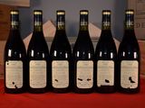 six bottles of wine are lined up on a red table cloth
