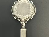 un miroir argenté posé sur une surface noire, muni d'une poignée argentée