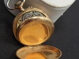 une petite montre de poche en or posée sur une surface noire
