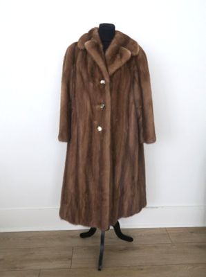 un manteau de fourrure marron posé sur un mannequin devant un mur blanc