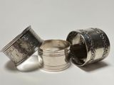three silver napkin rings with designs on them on a white surface