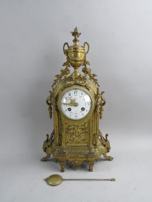 une horloge dorée posée sur une surface blanche, à côté d'une aiguille
