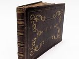 un vieux livre orné d'un motif doré, posé sur une surface blanche