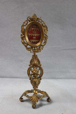 une image représentant une petite horloge en or posée sur un socle, avec une image rouge au centre