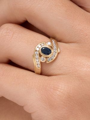 une photo représentant la main d'une femme portant une bague en or sertie d'un saphir bleu et de diamants blancs