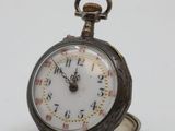 a silver pocket watch sitting on top of a white table