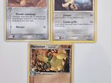 Trois cartes Pokémon sont posées sur une surface blanche, sur fond blanc.