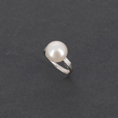 une bague en perles blanches et diamants sur une surface noire