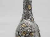 a silver and gold vase sitting on a white surface