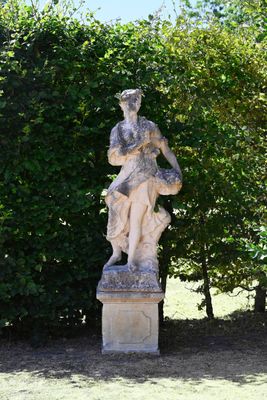 a statue of a woman sitting on a pedestal in the middle of a garden