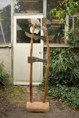 une sculpture représentant deux haches posées sur un socle en bois devant un bâtiment