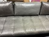 silver leather sofa with pillows on top of it in a store
