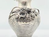 a silver vase with flowers on it on a white surface