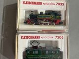 une paire de deux trains miniatures dans des boîtes en plastique, posés sur une surface blanche