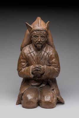 une photo représentant une statue d'un homme assis sur un tabouret