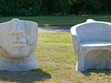 two stone sculptures of a man and a chair in the grass