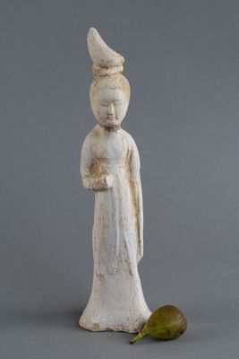 une vieille statue représentant une femme coiffée d'un chapeau, avec une poire posée par terre