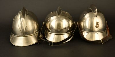 trois casques de pompier argentés posés sur une table noire