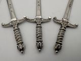 two silver metal swords with a skull on them on a white surface