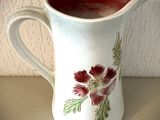 un pichet blanc orné de fleurs rouges, posé sur une table