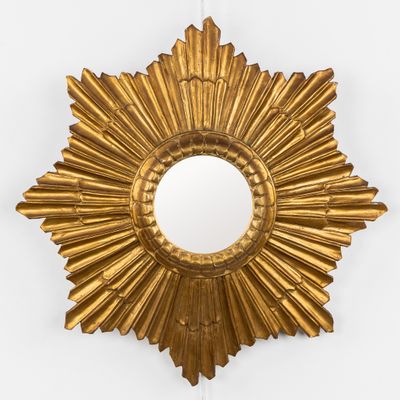 une photo d'un miroir doré en forme de soleil accroché au mur
