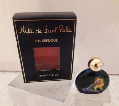un flacon de parfum dans une boîte transparente posée sur un comptoir, avec une boîte de parfum en arrière-plan