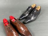 two pairs of brown shoes with red soles on a gray surface