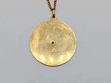 a close up of a gold disc pendant on a gold chain