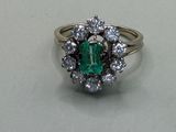 an emerald and diamond cluster ring on a white surface