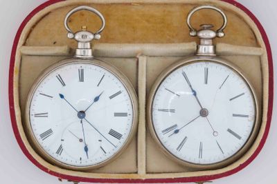two clocks sitting in a case on a white surface