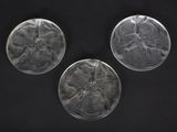 three clear glass plates with designs on them on a black surface
