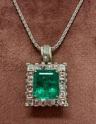 an emerald and diamond pendant on a brown velvet surface