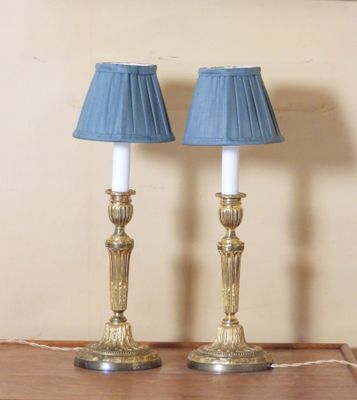 two lamps that are on a table with a picture on the wall in the background