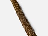 le bracelet en métal doré est posé sur un fond blanc