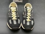 pair of black and white sneakers with yellow laces on a black surface