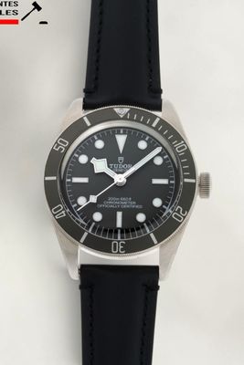 La montre est dotée d'un cadran noir et d'un bracelet en cuir noir.