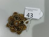 une broche en or posée sur une assiette blanche, avec une étiquette de prix