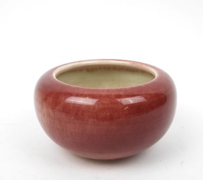 un vase rouge posé sur une surface blanche, avec un fond blanc