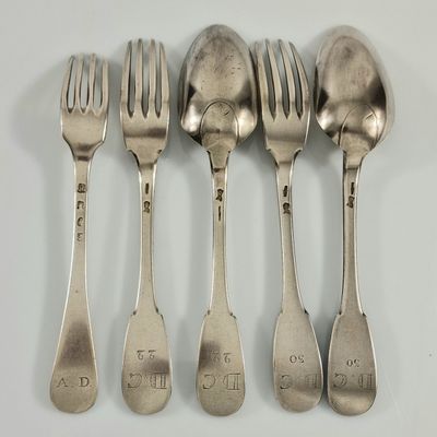 cinq cuillères en argent et une fourchette sont alignées sur une surface blanche