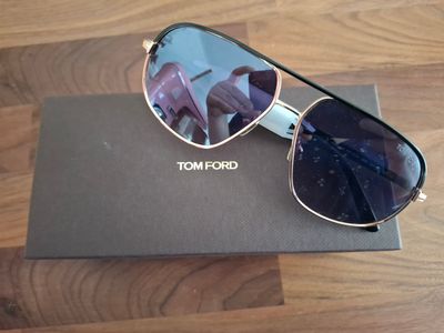 Lunettes de soleil Tom Ford avec leur étui, posé sur un parquet
