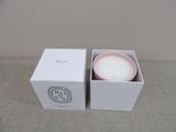 candle in a white box with a pink lid sitting on a table