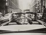 photographie en noir et blanc d'un couple au volant d'une décapotable dans une rue animée de la ville