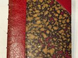 un gros plan d'un livre rouge et marron posé sur une surface blanche